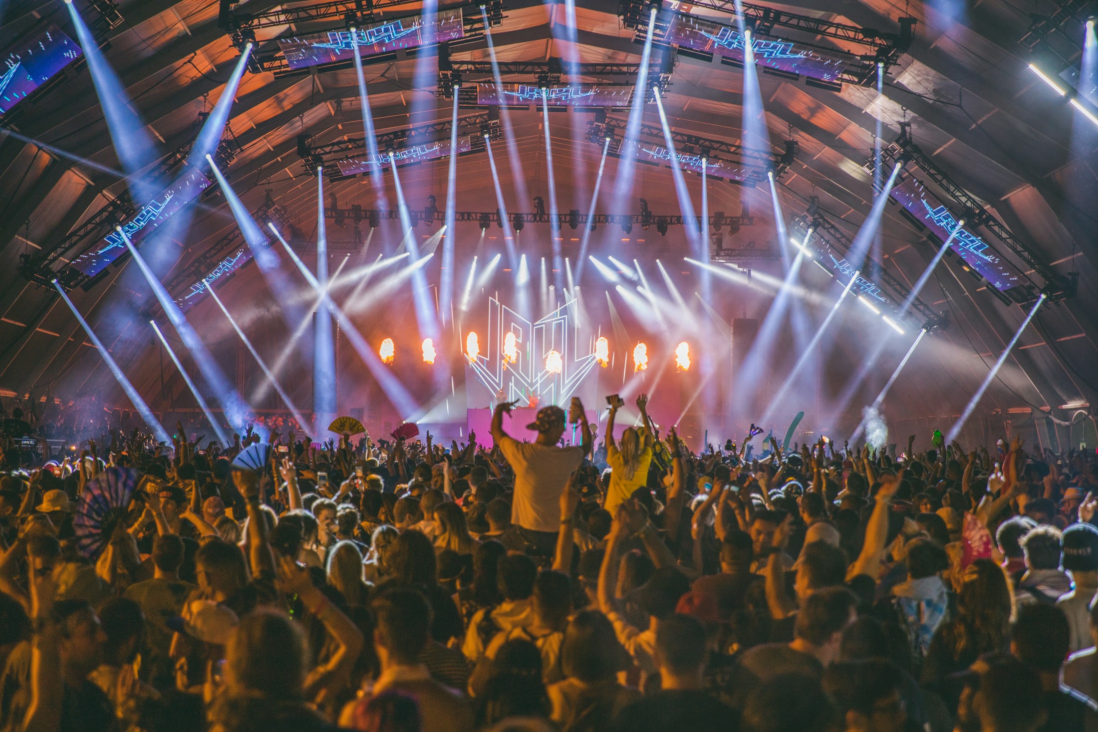 A live music crowd beneath sweeping stage lights